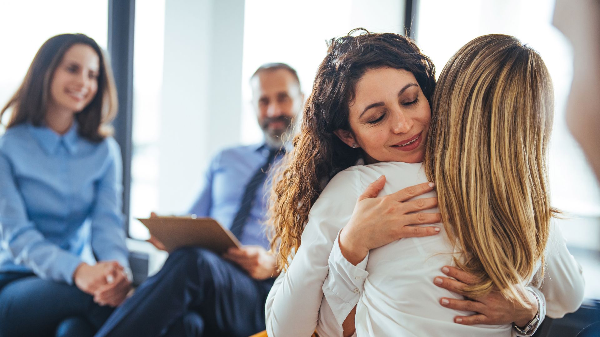 Residential treatment: Woman embracing another in supportive group therapy setting. Mental health and addiction recovery concept.