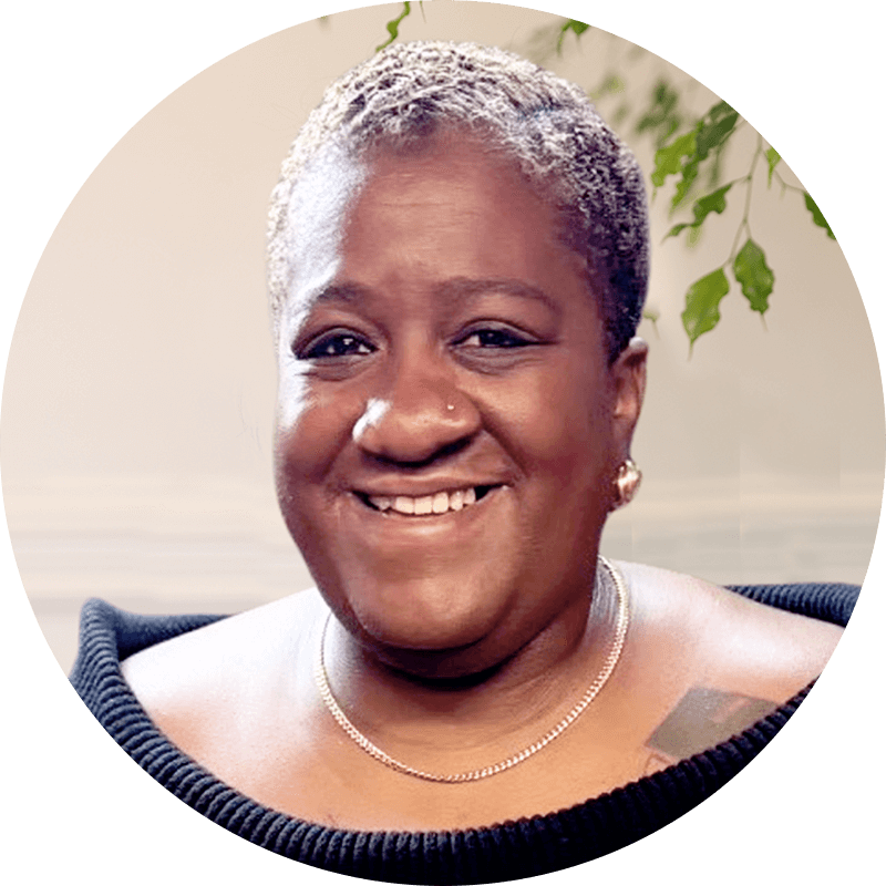 Stacia-Ponce-Rodriguez-1 - Dallas Mental Health Stacia Ponce Rodriguez portrait: Smiling woman with short gray hair, wearing a black top and gold chain.