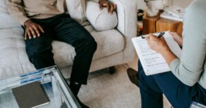 - Dallas Mental Health Therapist or counselor taking notes on a clipboard as a client sits on a sofa during a session.