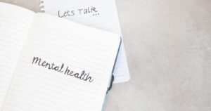 Notebook open to a page that says 'mental health' in cursive, with a 'Let's Talk' note nearby on a light background.