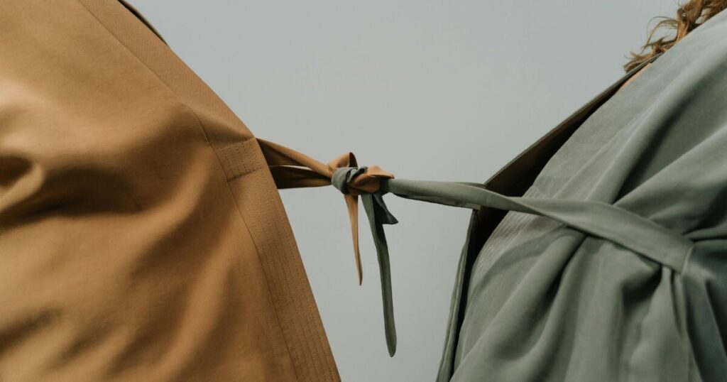 image - Dallas Mental Health Close-up of two fabric garments—a tan coat and a sage-green coat—knotted together at the center against a neutral background.